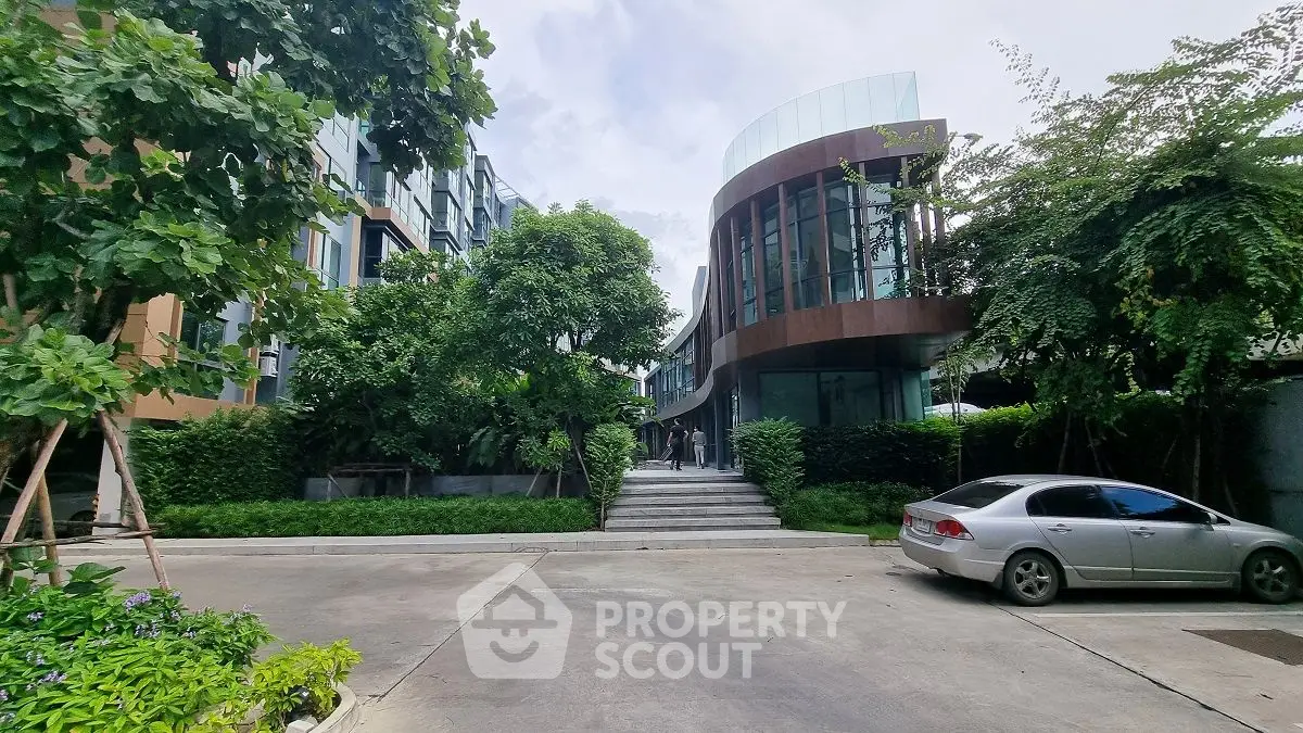Modern architectural building with lush greenery and parked car in urban setting.