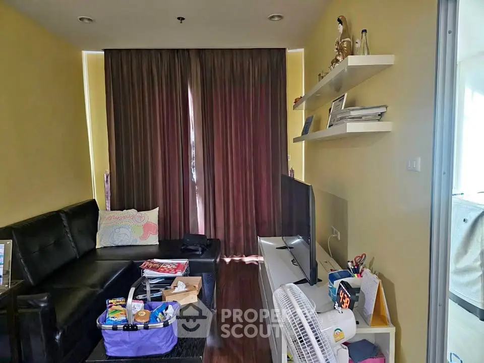 Cozy living room with black leather sofa, TV, and shelves in a modern apartment.
