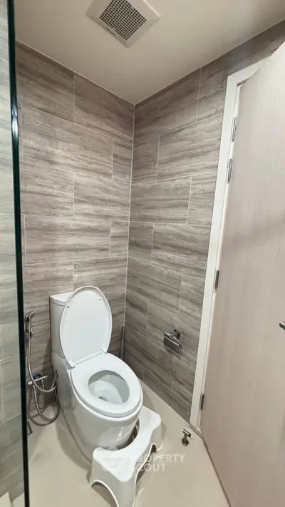 Modern bathroom with sleek design and neutral tones, featuring a toilet and stylish wall tiles.