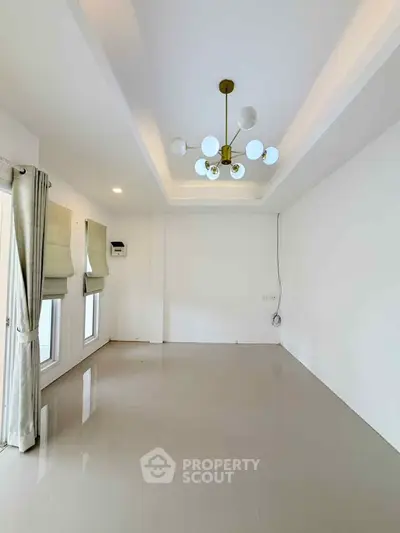 Spacious empty room with modern chandelier and large windows, perfect for customization.