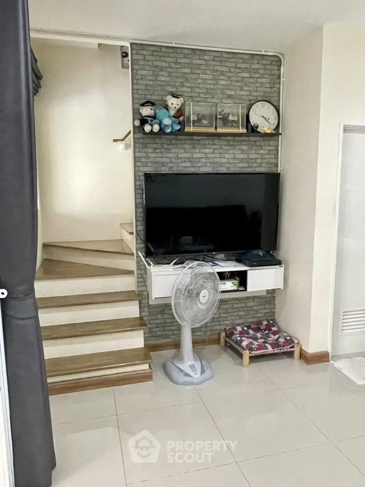 Modern living room with TV, fan, and staircase in stylish home interior.