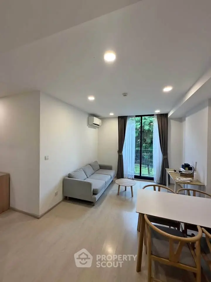 Modern living room with cozy sofa and dining area, featuring large windows with garden view.