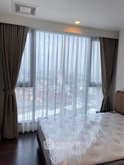 Modern bedroom with large window offering stunning city view, featuring elegant curtains and a comfortable bed.