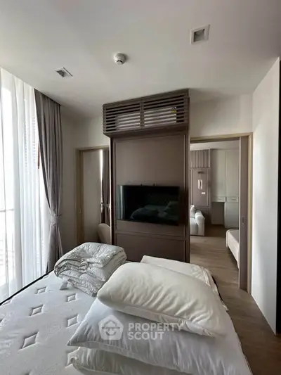 Modern bedroom with elegant decor and natural light, featuring a stylish TV partition and cozy bedding.