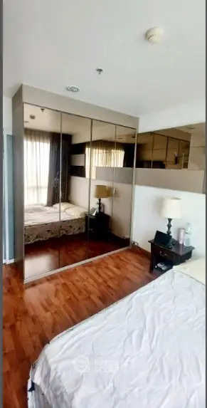 Spacious bedroom with mirrored wardrobe and wooden flooring in modern apartment.