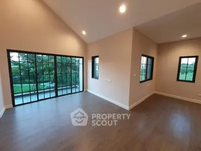 Spacious modern living room with large windows and wooden flooring, offering a serene view.