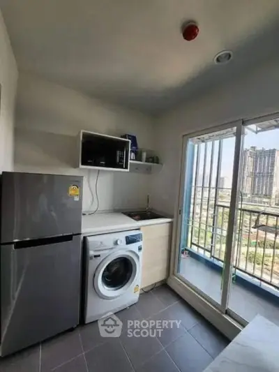 Modern kitchen with washing machine and fridge, featuring balcony access and city view.