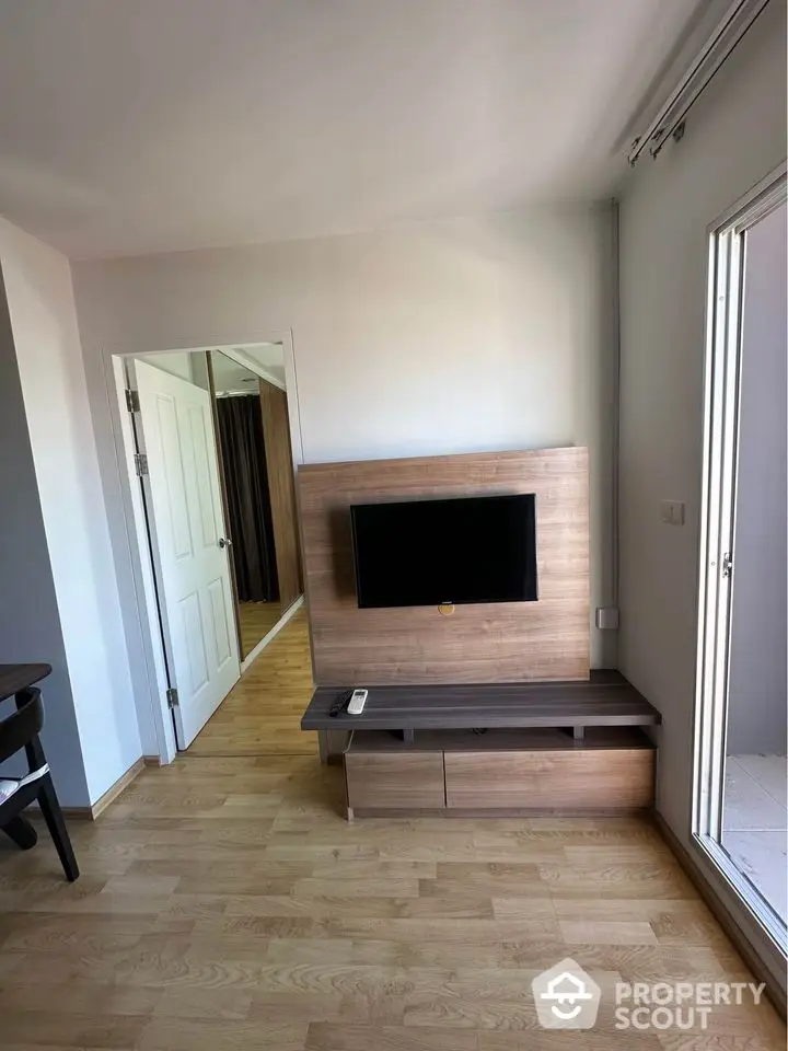 Modern living room with wooden flooring and wall-mounted TV, open door to adjacent room.