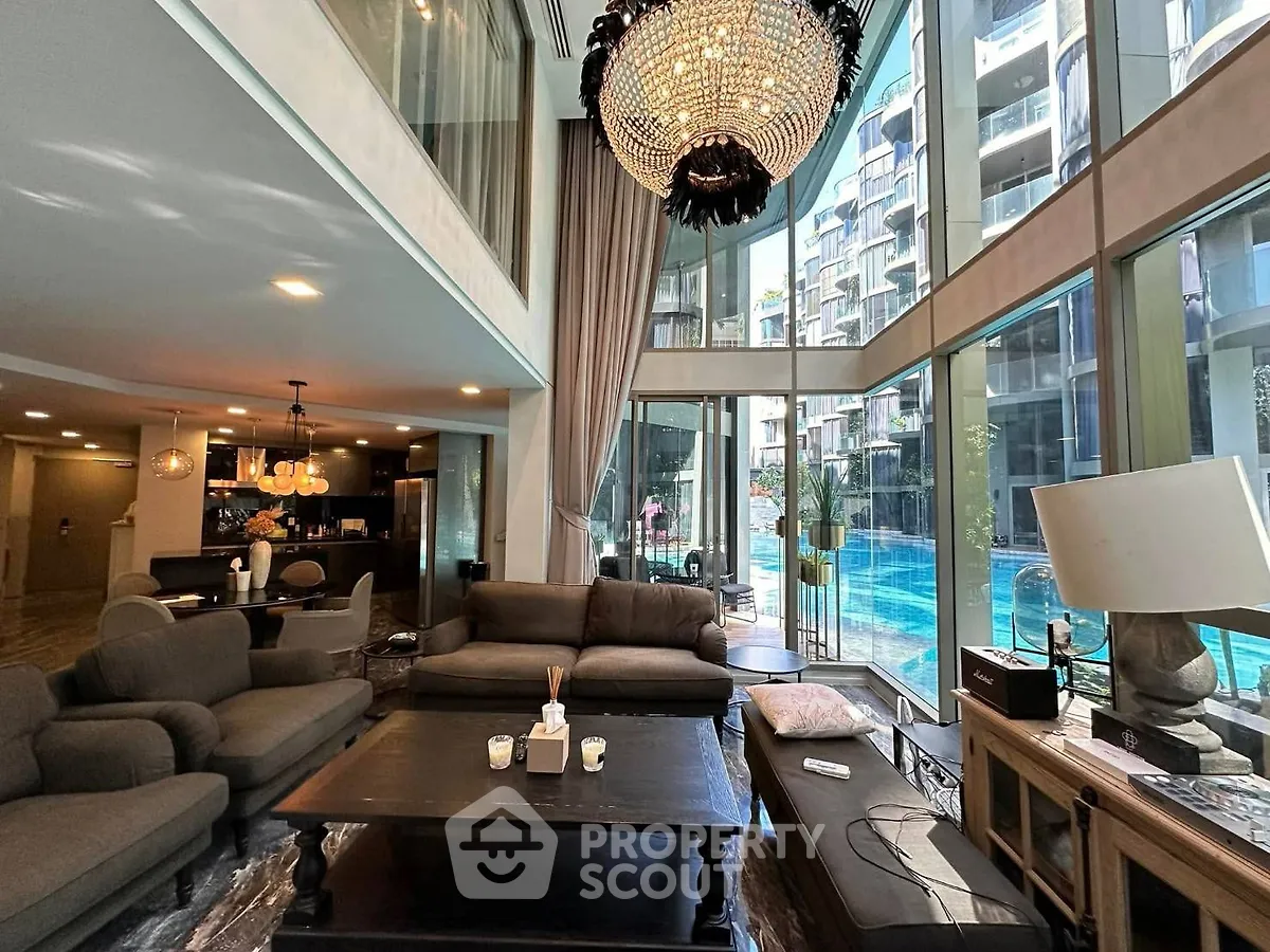 Luxurious living room with floor-to-ceiling windows overlooking a stunning pool view, featuring elegant decor and chandelier.