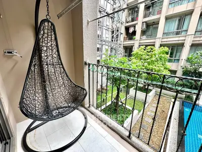 Charming balcony with hanging chair overlooking lush garden and pool in modern apartment complex.