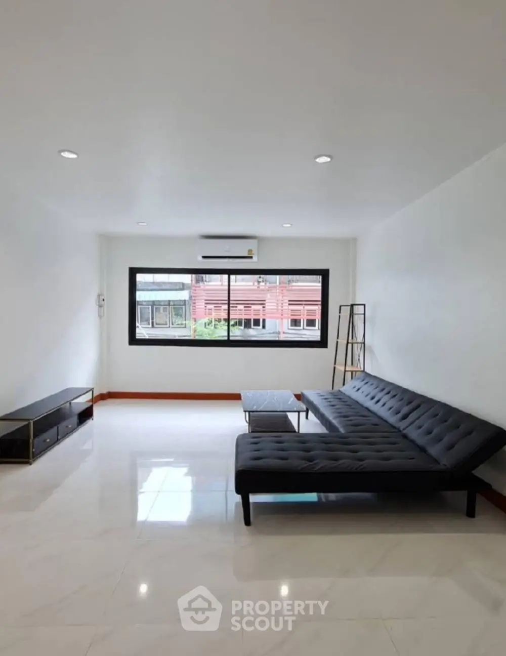 Spacious modern living room with sleek black sofa and large window view.