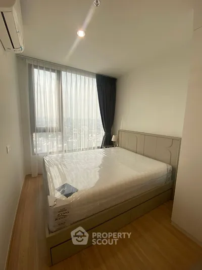 Modern bedroom with large window and city view, featuring a comfortable bed and elegant curtains.