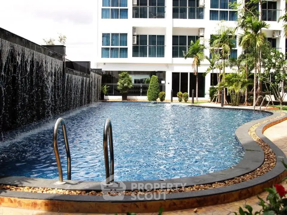Luxurious apartment complex with stunning pool and waterfall feature, surrounded by lush greenery.