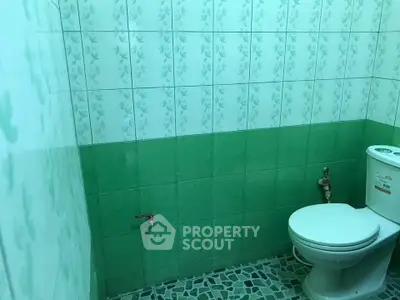 Compact bathroom with green and white tiled walls and a modern toilet.