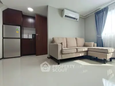Modern living room with beige sofa and natural light, adjacent to compact kitchen.