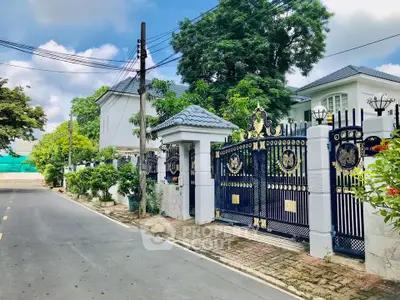 Elegant gated entrance of a luxurious residential property with ornate ironwork and lush greenery.