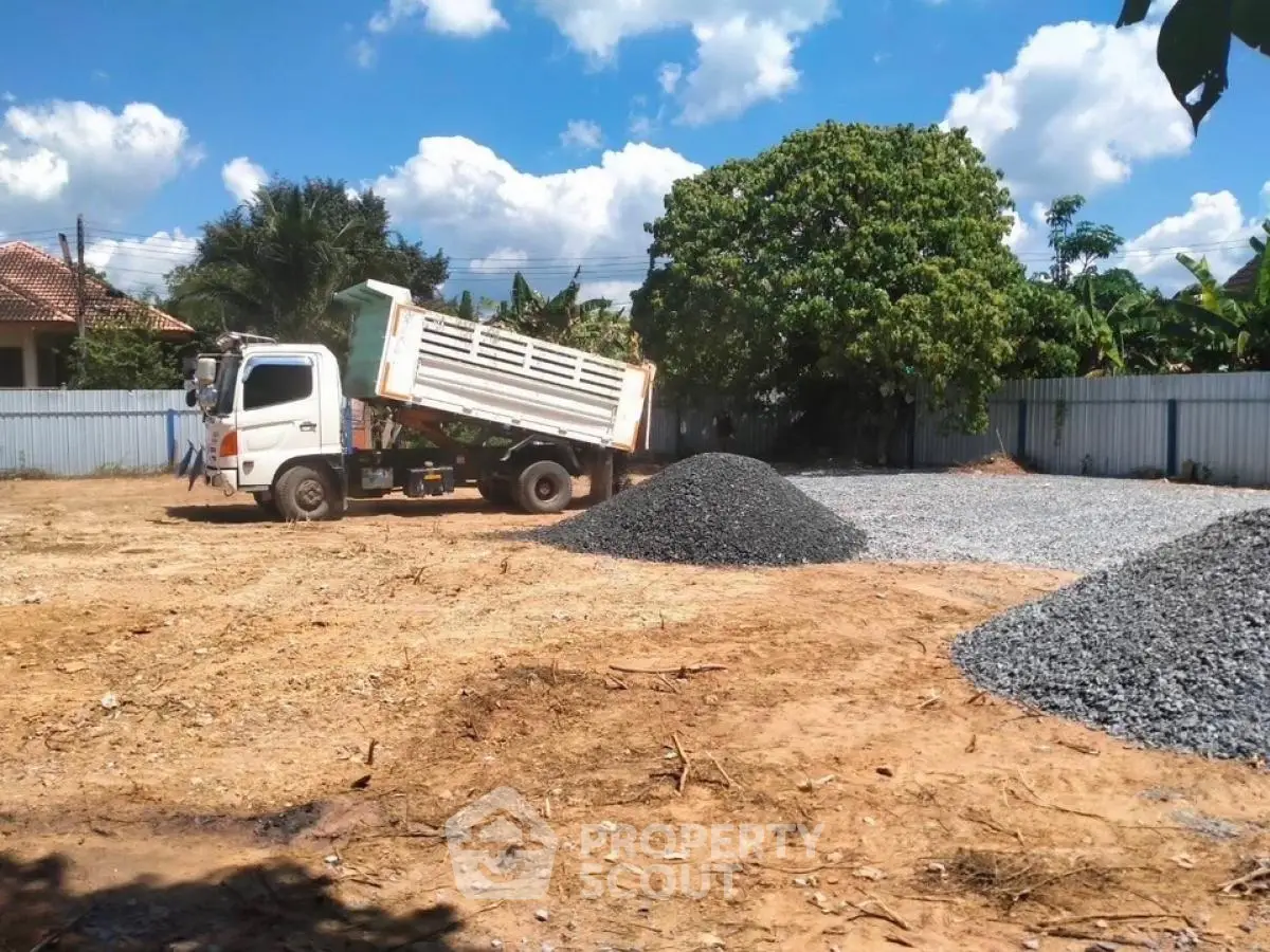 Vacant land with construction truck and gravel piles under clear blue sky.