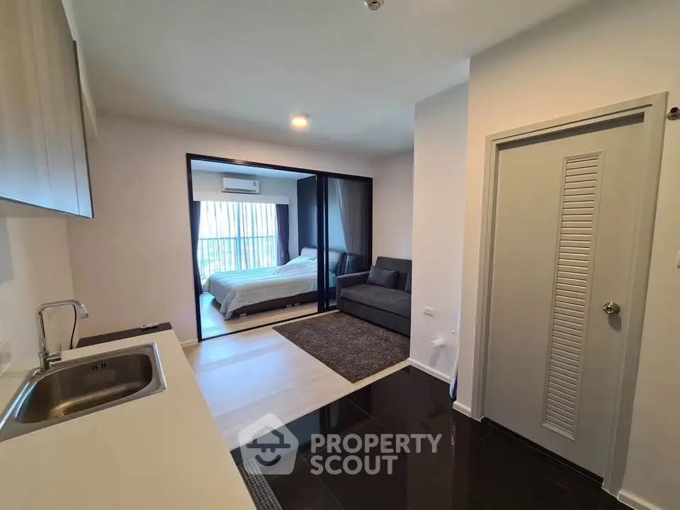 Modern open-layout apartment with sleek kitchen and cozy living area leading to a bright bedroom.
