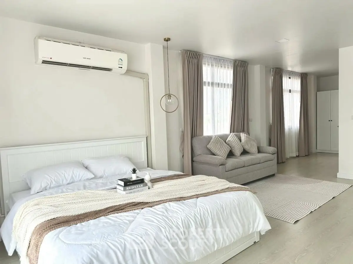 Spacious bedroom with modern decor and cozy seating area, featuring natural light and elegant curtains.