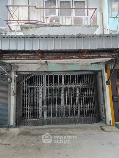 Commercial property with metal gate and upper balcony in urban setting.