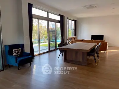 Spacious living room with large windows and elegant dining area overlooking greenery.