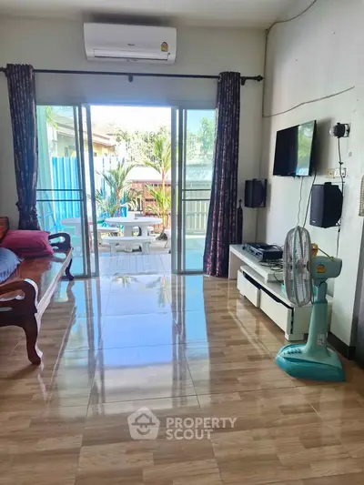 Spacious living room with sliding glass doors leading to a balcony, featuring modern furnishings and air conditioning.