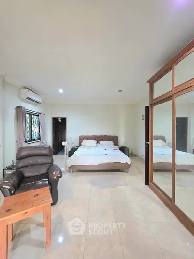 Spacious bedroom with large mirrored wardrobe and comfortable seating area.