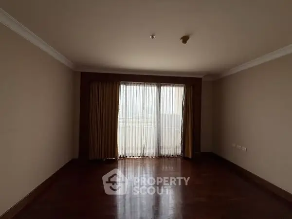 Spacious empty living room with wooden floors and large window with curtains.