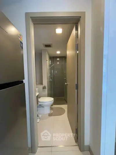 Modern bathroom with sleek design and adjacent kitchen area featuring a stainless steel fridge.
