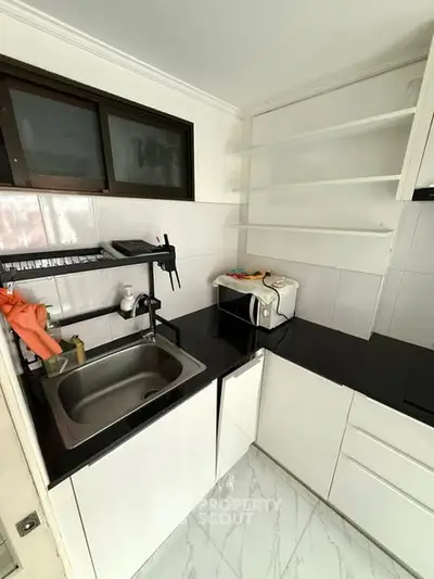 Modern kitchen with sleek black countertops and white cabinetry, featuring a compact layout and built-in appliances.