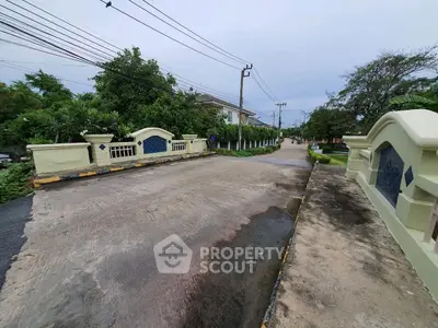 Charming residential street with lush greenery and elegant entrance bridge.