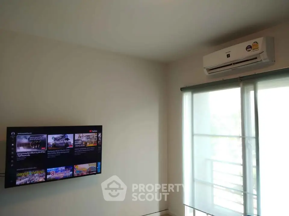 Modern living room with wall-mounted TV and air conditioning, featuring a bright window view.