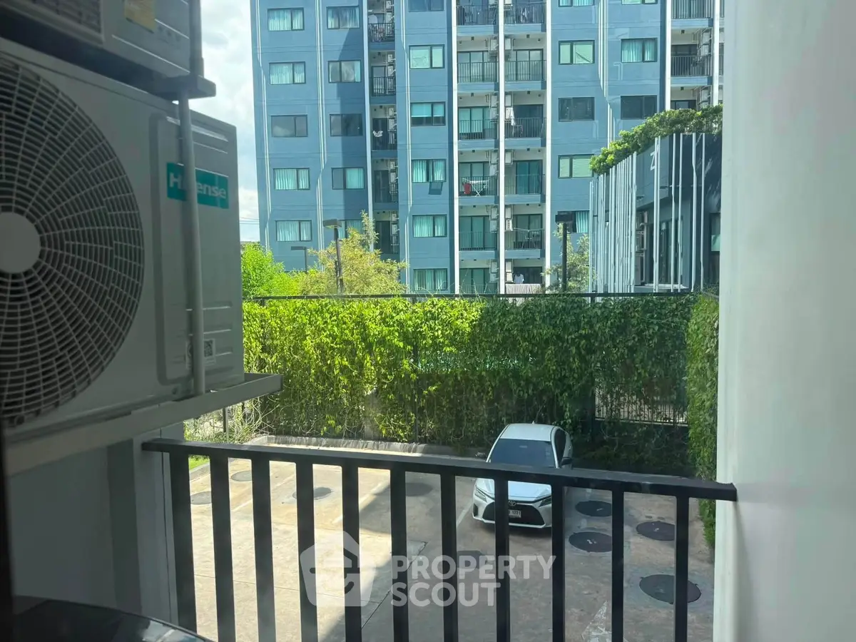 Modern apartment view with lush greenery and parked car in urban setting.