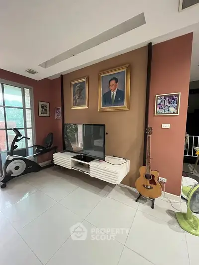 Modern living room with exercise bike, TV, and guitar, showcasing sleek design and natural light.