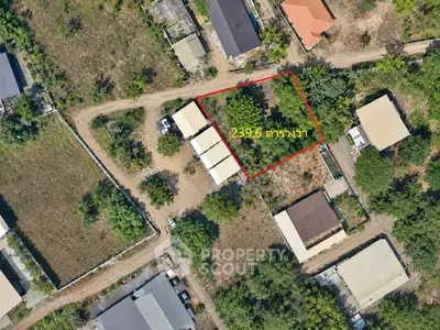Aerial view of a plot of land outlined in red, surrounded by residential buildings and greenery.