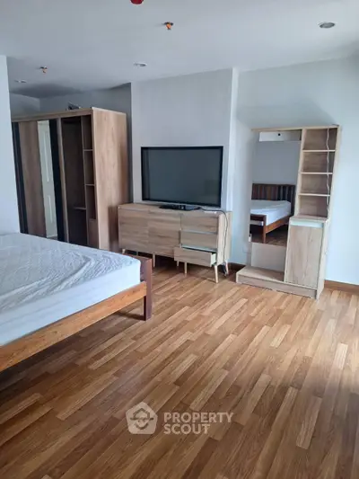Spacious bedroom with wooden flooring and modern furniture, featuring a large bed and flat-screen TV.