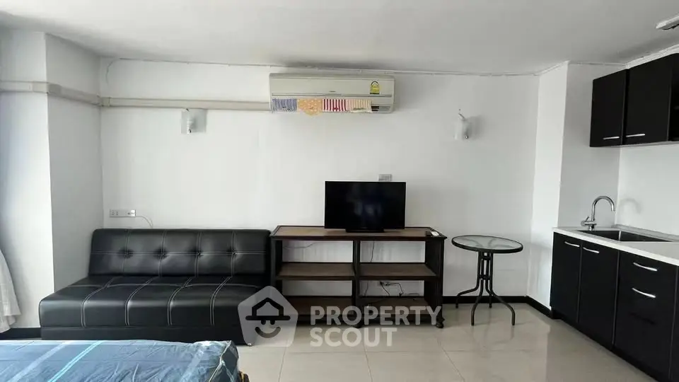 Modern studio apartment with sleek black furniture and compact kitchenette.
