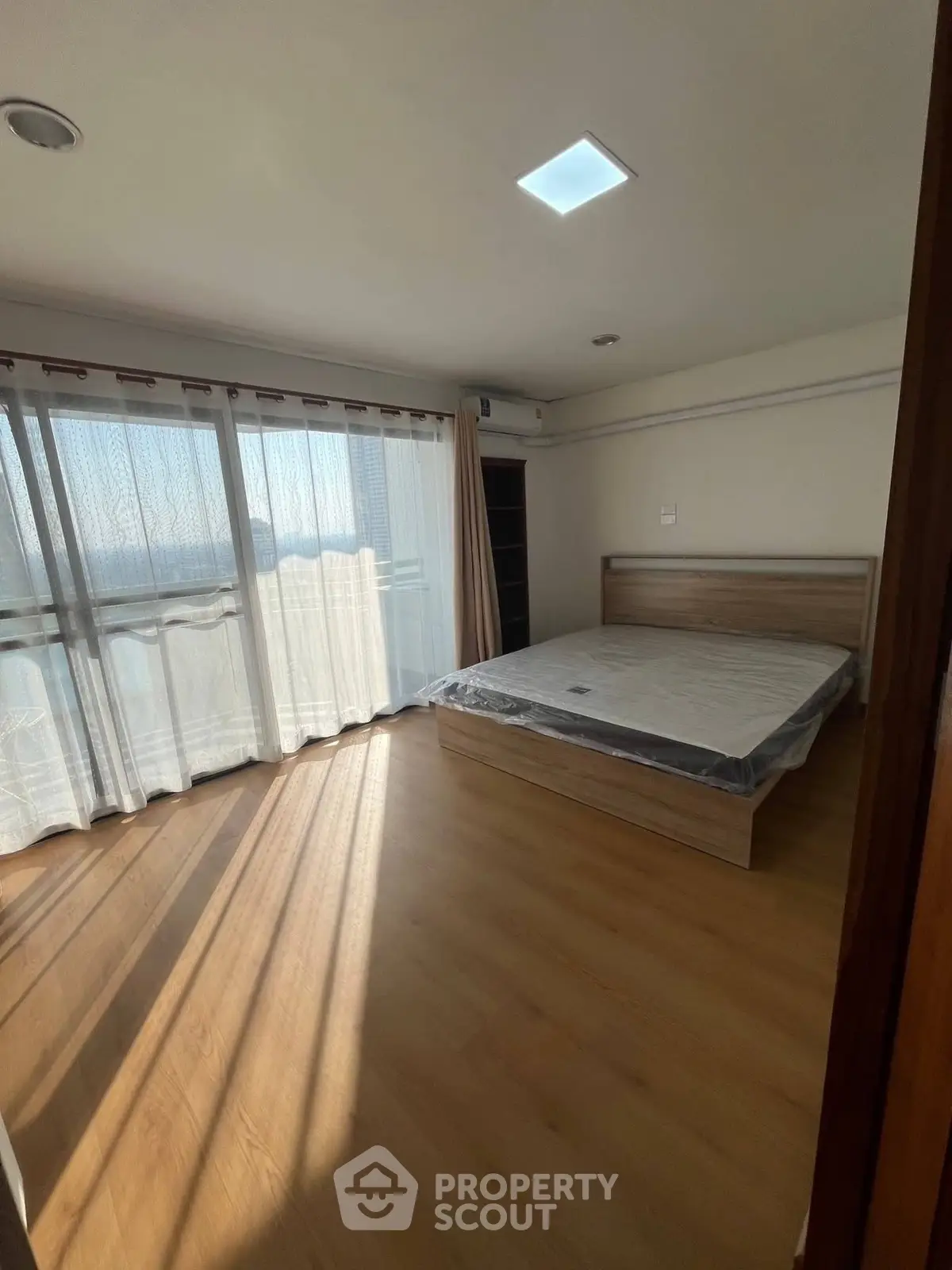Spacious bedroom with large windows and natural light, featuring a modern bed and wooden flooring.