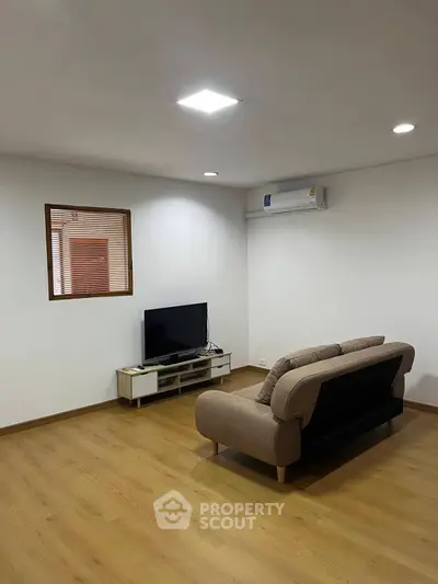Spacious living room with modern sofa and TV setup, featuring sleek wooden flooring and air conditioning.