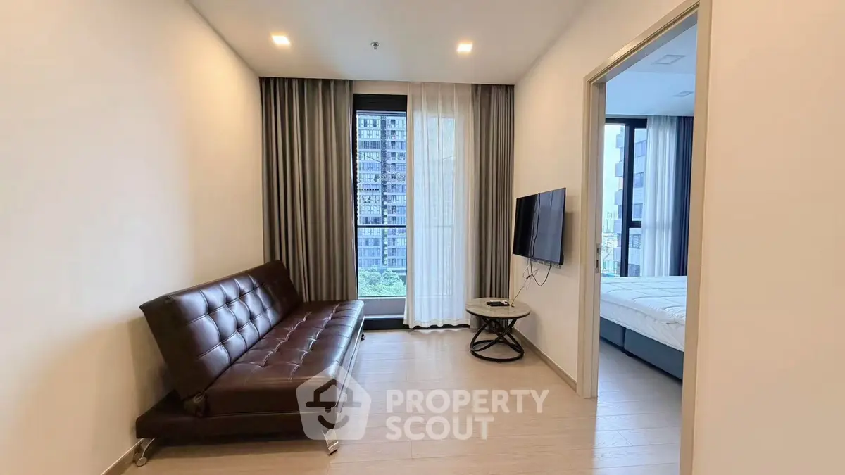 Modern apartment living room with sleek leather sofa and wall-mounted TV, adjacent to a cozy bedroom.