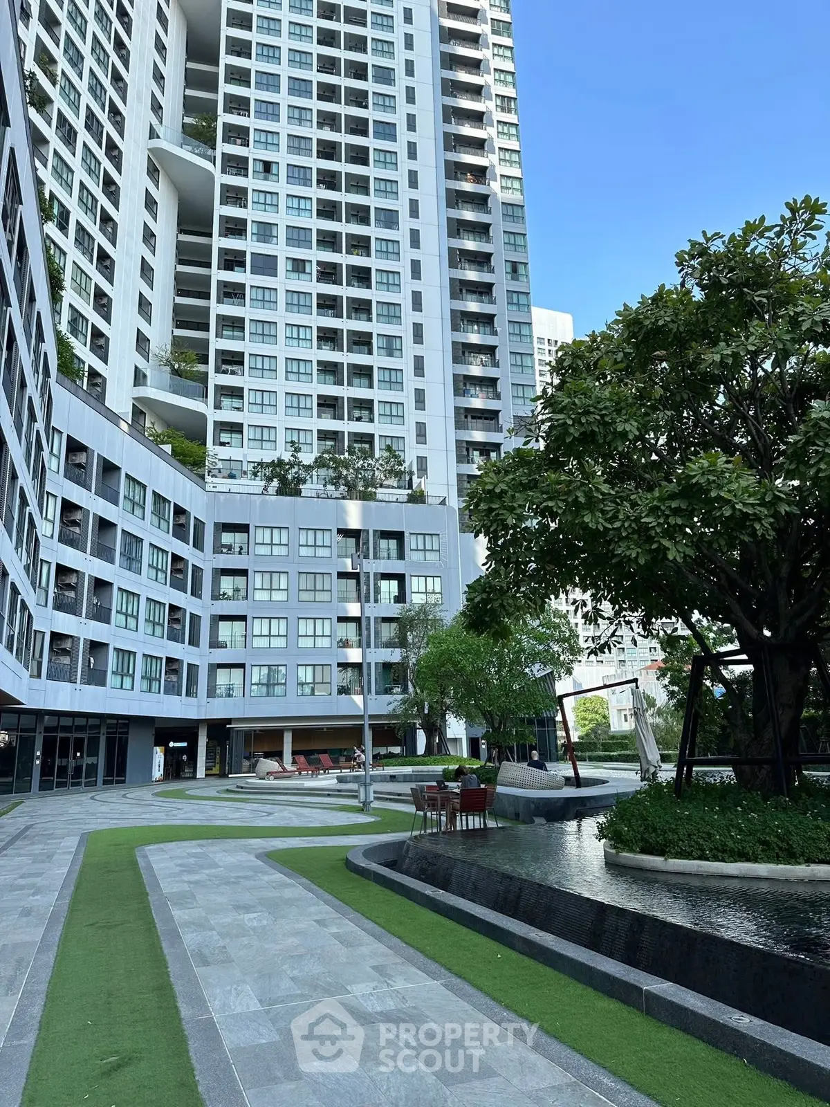 Modern high-rise residential building with landscaped garden and seating area.