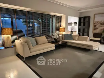 Elegant living room with modern beige sofas, stylish lamps, and large window with blinds.