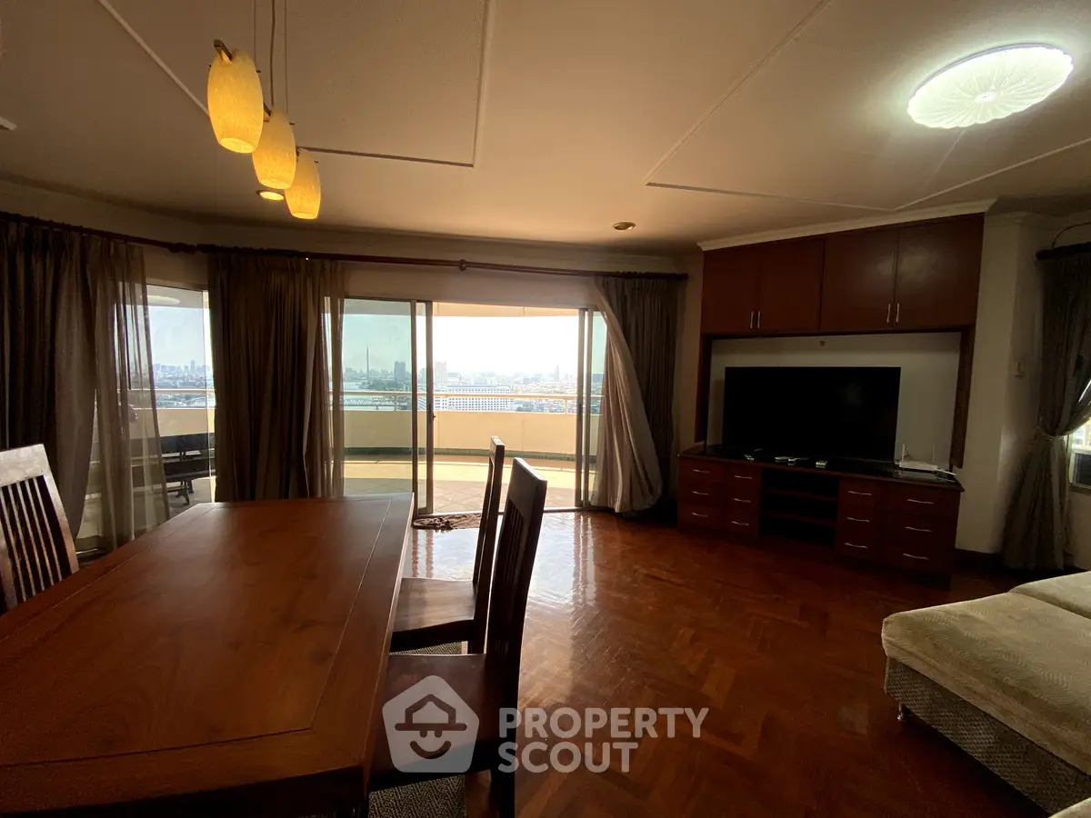 Spacious living room with large balcony and city view, featuring elegant wooden furniture and ample natural light.