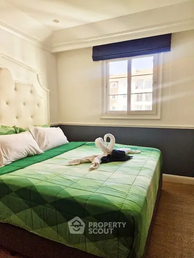 Cozy bedroom with green bedding and window view, perfect for relaxation.