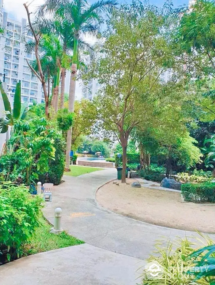 Lush garden pathway in modern residential complex with tall palm trees and vibrant greenery.