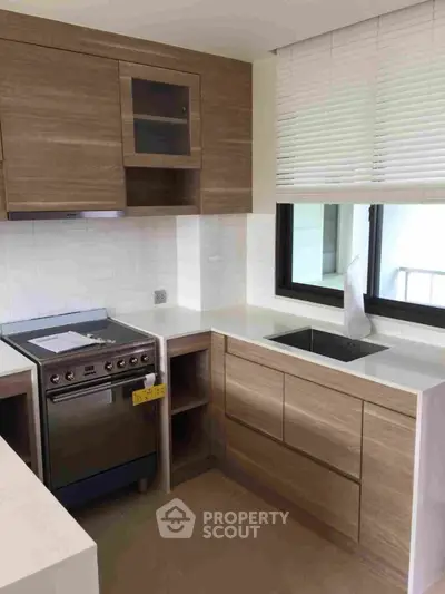 Modern kitchen with sleek wooden cabinetry and built-in appliances, complemented by white countertops and a bright window.