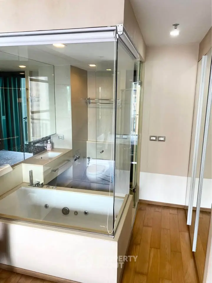 Modern bathroom with glass-enclosed bathtub and sleek wooden flooring