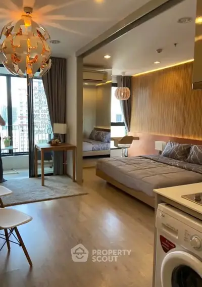 Modern studio apartment with stylish decor and balcony view, featuring a cozy bed and in-unit washing machine.