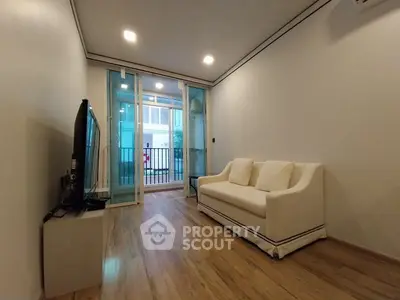 Modern living room with sleek wooden flooring and cozy white sofa, featuring a large TV and balcony access.
