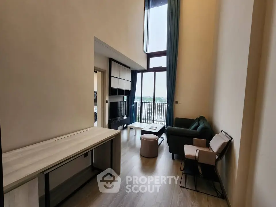 Modern living room with high ceiling and large windows offering natural light and a cozy seating area.